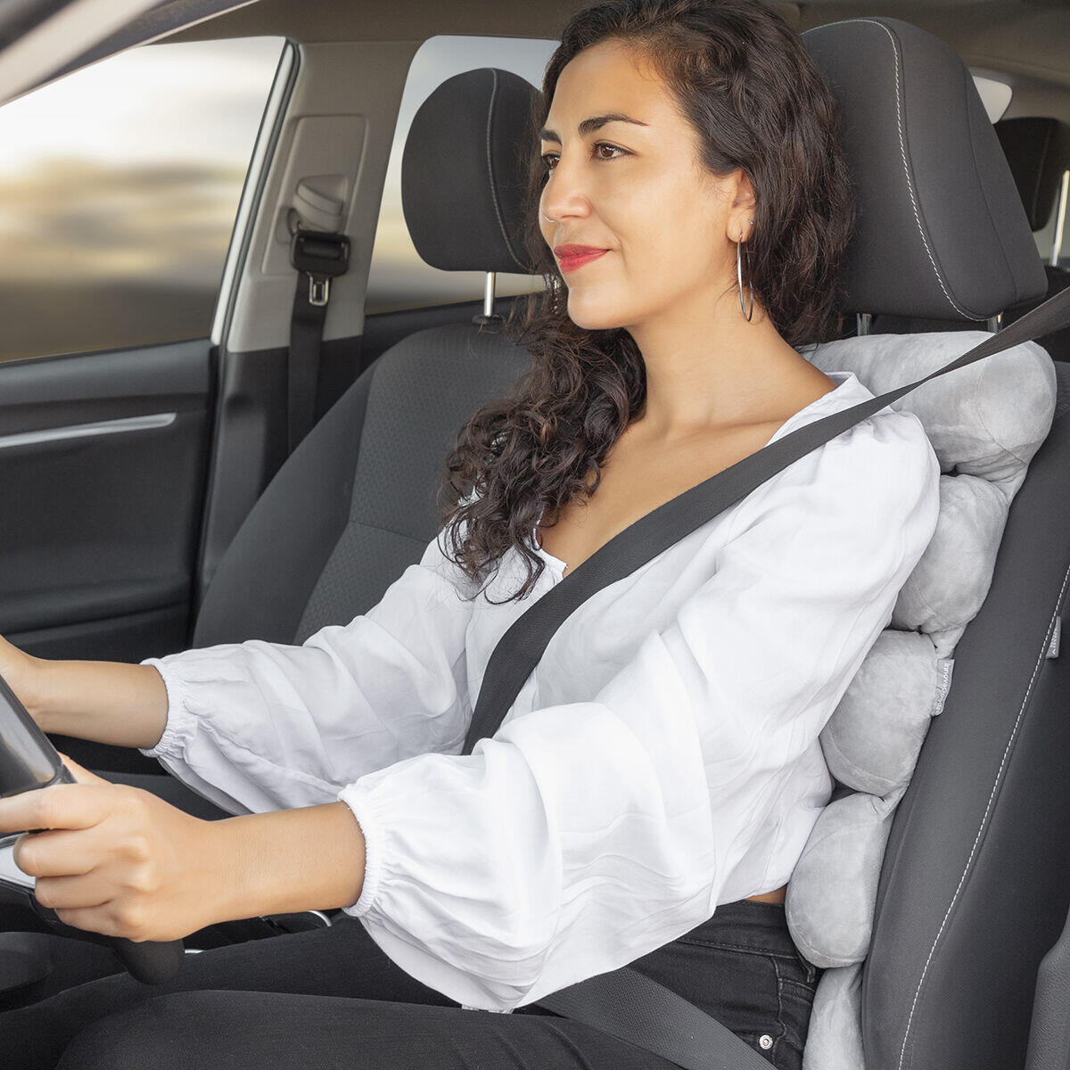 Mujer sentada sobre el asiento de un coche usando la almohada modular multifunción Rollow

