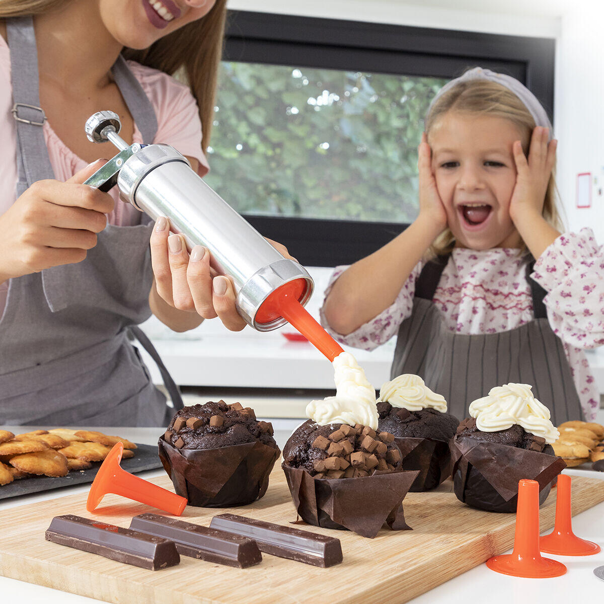 Mamá usando la Máquina para Hacer Galletas y Manga Pastelera 2 en 1 Prekies InnovaGoods para añadir crema pastelera sobre magdalenas