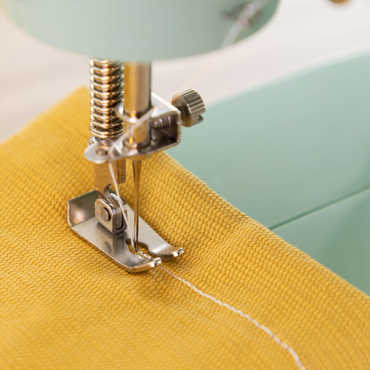 Mini máquina de coser portátil en uso , cosiendo una tela amarilla