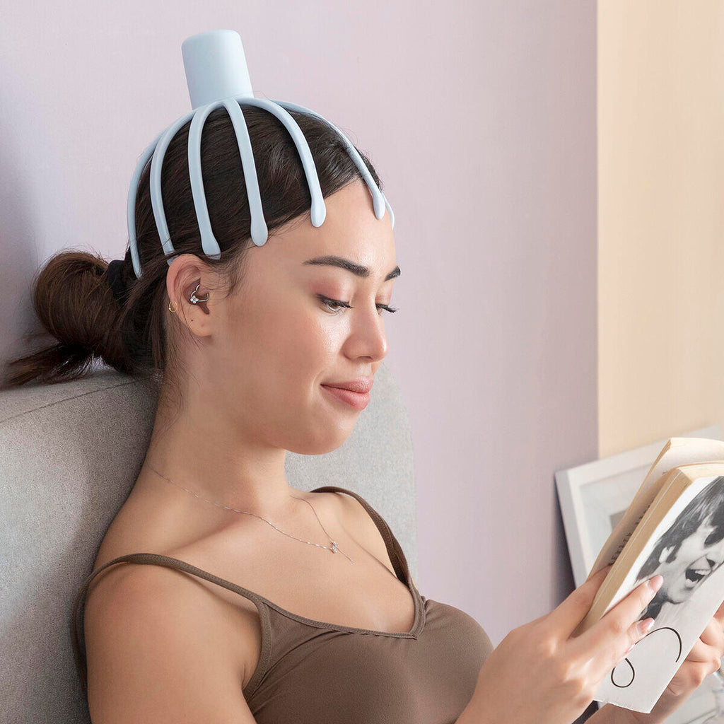 mujer sonriente usando el masajeador de cabeza recargable Helax mientras lee un libro