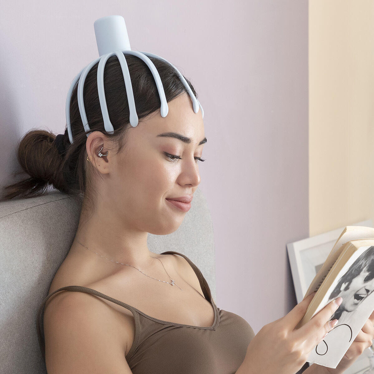 mujer sonriente usando el masajeador de cabeza recargable Helax mientras lee un libro
