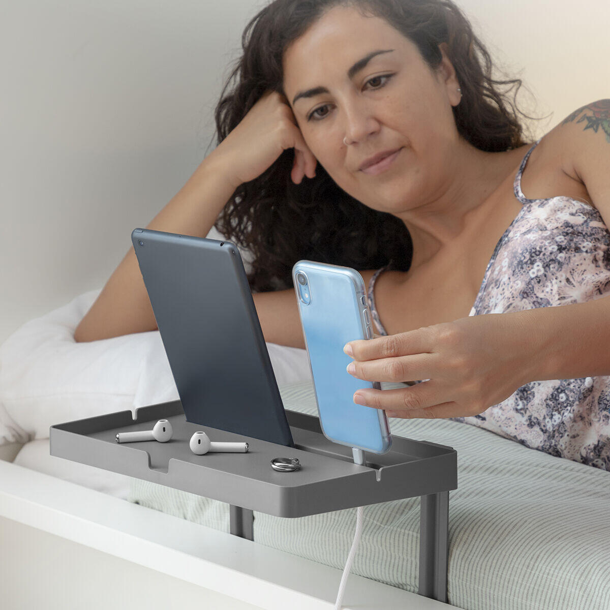 mujer usando estante organizador universal para cama mientras observa su móvil
